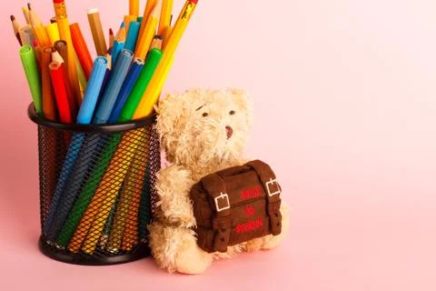 Brown teddy bear with school backpack and glass with felt-tip-pens, pink back 写真素材