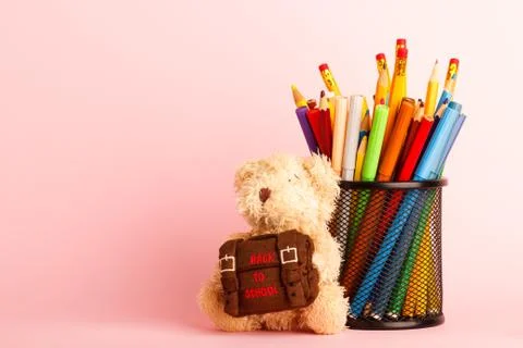 Brown teddy bear with school backpack and glass with felt-tip-pens, pink back 库存照片