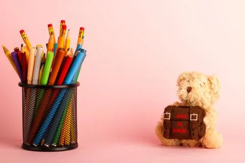 Brown teddy bear with school backpack and glass with felt-tip-pens, pink back Stock Photos