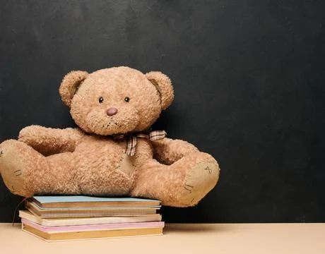 Brown teddy bear sitting on a stack of colorful books symbolizing childhood.. Stock Photos