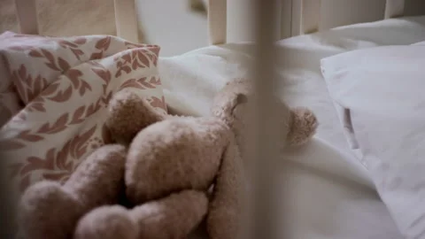 Brown Teddy Bear Soft Toy Lying in Empty Baby Cot with White Bedding Stock Footage 281240077