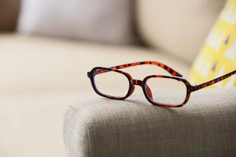 Brown tortoiseshell reading glasses on sofa armrest, vision correction and ey Stock Photos