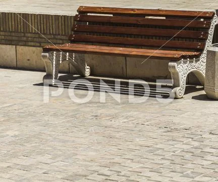 Brown wooden bench and a gray urn on the sidewalk in the city Stock Photos