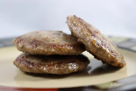 Browned sausage patties stacked on saucer plate Stock Photos