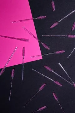 Brows brushes are scattered on a black background with a pink sheet of pape.. Stock Photos