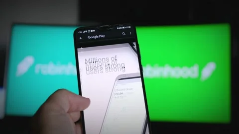 Browsing Robinhood app on Play Store to monitor equities rates for trader broker Stock Footage 141420583