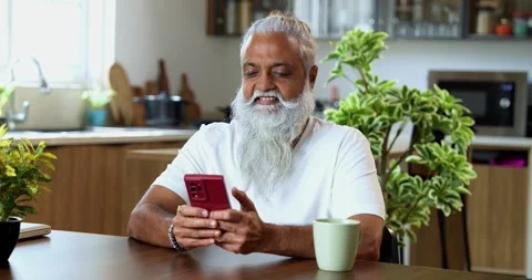 Browsing smartphone at breakfast, stylish Indian mid age man in modern kitchen Stock Footage 342778721