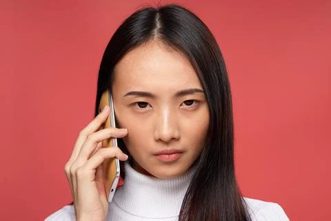 Brunette asian appearance talking on the phone technology studio red background Stock Photos