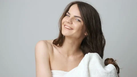 Brunette in the bathroom stands in front of a mirror and wipes her wet hair with Stock Footage 132966183