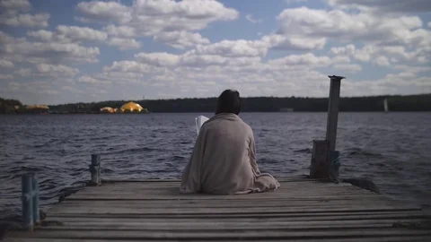 Brunette in blanket sits on old wooden pier and reads a book against the Stock Footage