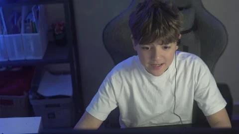 Brunette boy with earpiece in ear on gaming computer chair playing games online Stock Footage 305651065