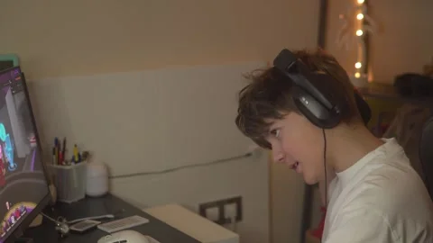 Brunette boy in headphones playing computer game in the evening, side view Stock Footage 304867072