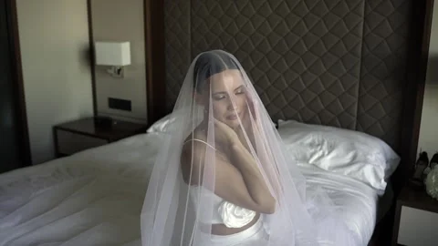 Brunette bride sitting on a double bed and posing while looking at the camera Vidéo 261739475