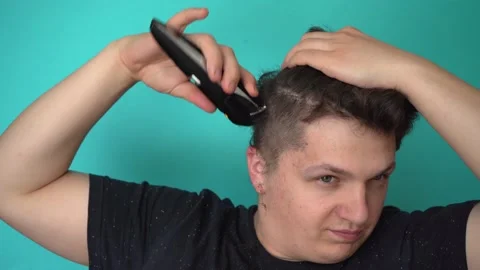 Brunette cuts himself with electric trimer. Smiles to himself Blue background 4K Stock-Footage 132655880