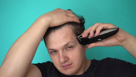 Brunette cuts himself with electric trimer. Smiles to himself. Blue background Stock-Footage 132655893