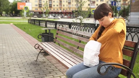 Brunette eating a hamburger on a bench near the road Stock Footage