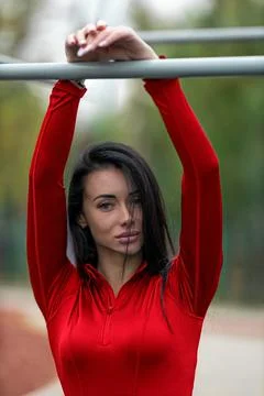 Brunette enjoying exercise at stadium while hanging on a bar in a red top during Stock Photos