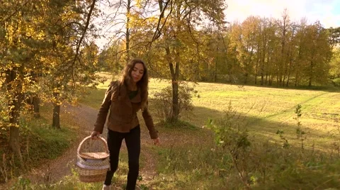 Brunette girl in brown jacket with a basket walking uphill in autumn woods Stock Footage