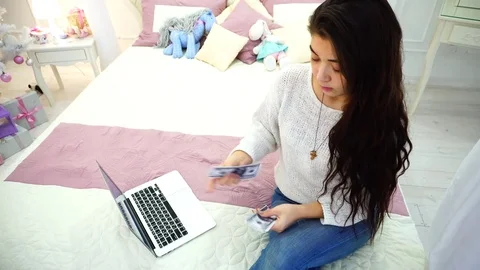 The brunette girl engaged in finances and solves money issues, sitting on bed in Stock Footage