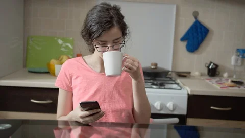 Brunette girl sitting in the kitchen using her phone while having breakfast Stock Footage 130060074