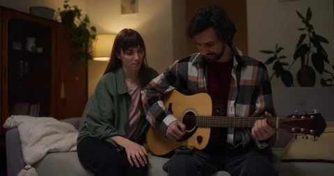 Brunette Guy Uses Tabs To Play Guitar While His Girlfriend Listens To Him In Stock Footage 318079528