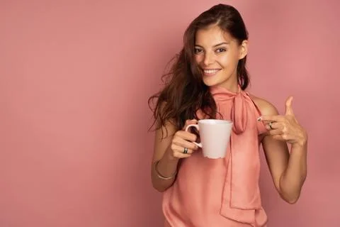 A brunette holding a mug in her hand and points the fingers of her other hand at Stock Photos