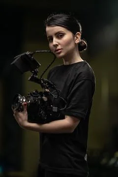 Brunette holds camera while posing indoors at evening in a well lit space Stock Photos