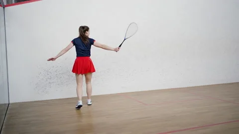Brunette lady hits ball with racket standing on squash court Stock Footage 228749817