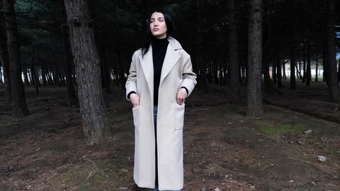 Brunette in light coat walks in pine forest slow motion Stock Footage 105293563