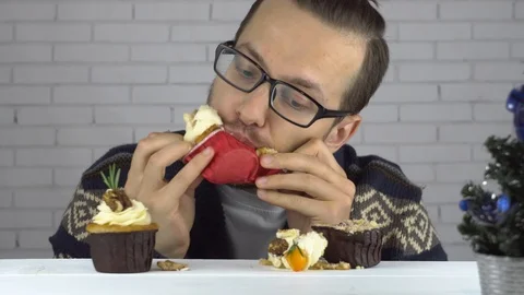 Brunette man eats cupcakes with greed 動画素材 99705844