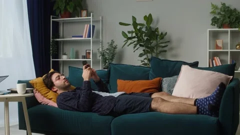 Brunette man lying on sofa and chatting with friends using smartphone in living Stock Footage 157235264