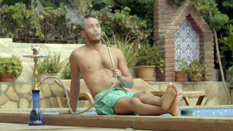 Brunette man smokes hookah by the pool. Stock Footage 144317097