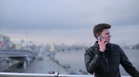 Brunette man talking on mobile phone on a background of the urban river Stock Footage 61430889