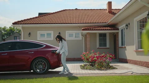 Brunette pulls the wire to the red electric car to charge it, talking on phone Stock Footage 244326580