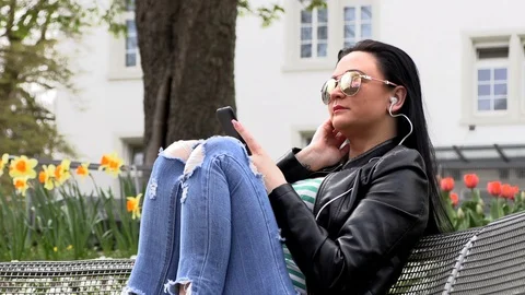 Brunette sits on a street bench and listens to music Stock-Footage 106915972