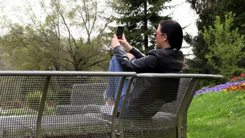 Brunette sits on a street bench and listens to music Stockbeeldmateriaal 106916015