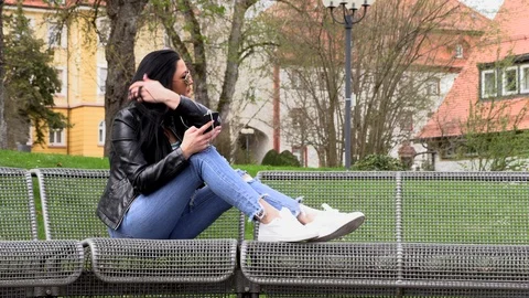 Brunette sits on a street bench and listens to music Vídeos de archivo 106952193