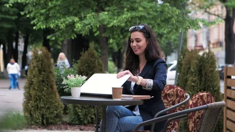 Brunette sitting on summer terrace in cafe and working on laptop 库存影片 75473370