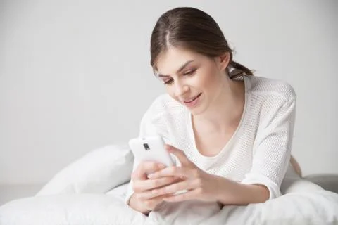 Brunette smiling while using smartphone on pillow at home Stock Photos