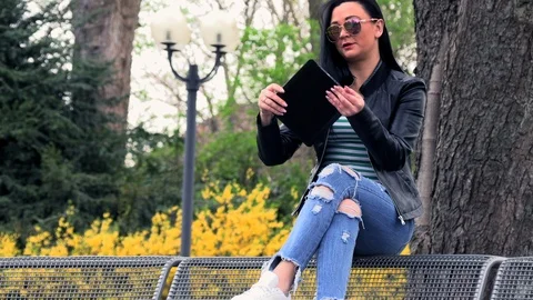 Brunette on a street bench with a tablet Stockbeeldmateriaal 106892387