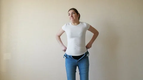 Brunette struggles to pull on her jeans and can't button them Stock Footage 122728030