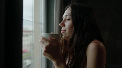 A brunette with a white mug is standing by the window Stock Footage 200990394