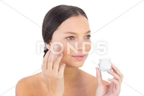 Brunette woman spreading beauty cream on her cheek Stock Photos
