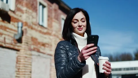 Brunette woman using device while standing with coffee cup on blurred background Stock-Footage 266783291