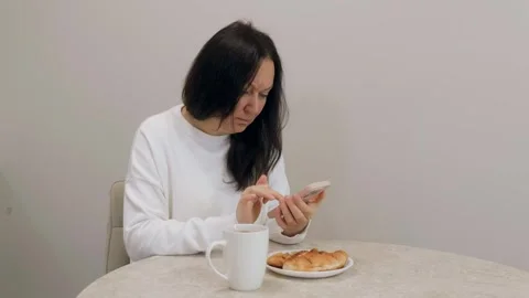 Brunette woman using smartphone while having breakfast at home Stock Footage 306565580