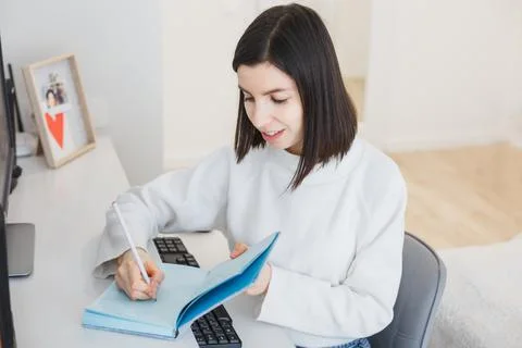 The brunette writes in a notebook while sitting at her desk Stock Photos