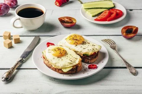 Bruschettas with vegetables and fried egg on white plate, cup of coffee and some Stock Photos