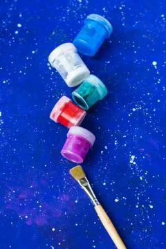 Brush and several jars of different colors paint on galaxy-blue background Stock Photos