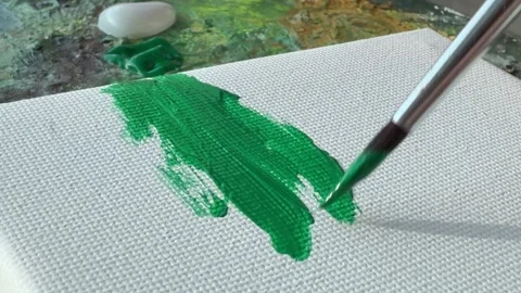 A brush applying green paint on a textured canvas surface. 库存影片 343300799