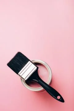 Brush with black handle on open can of pink paint on pastel background. Stock Photos